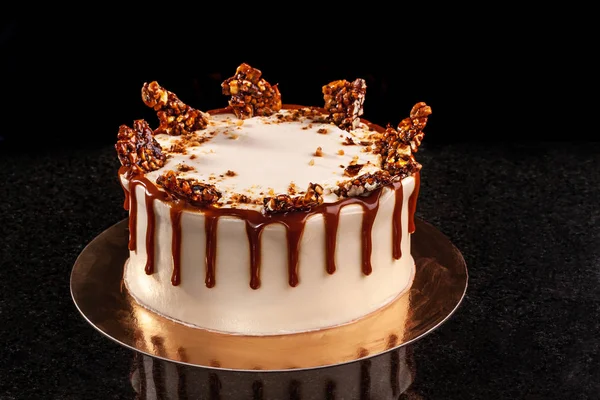 Torta redonda blanca con arroz inflado de caramelo y chocolate sobre una bandeja redonda sobre fondo negro — Foto de Stock