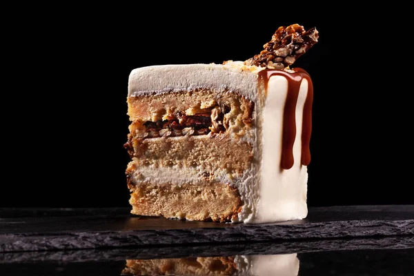 Pedazo de pastel blanco con caramelo y arroz inflado con chocolate sobre una bandeja negra sobre fondo negro —  Fotos de Stock