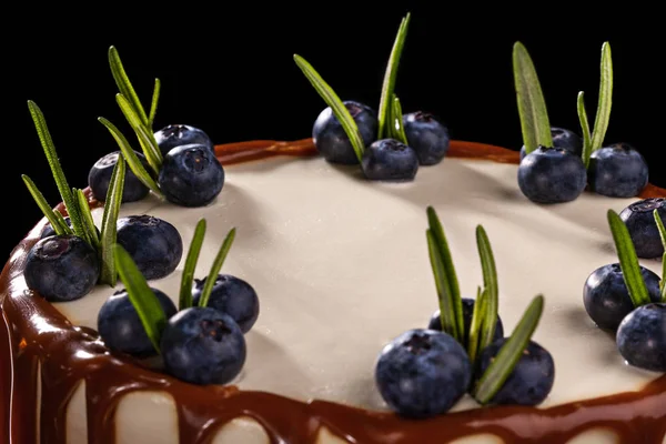 Chocolate cake with blueberries on a black background, decorated with small green leaves and fresh berries — Stock Photo, Image