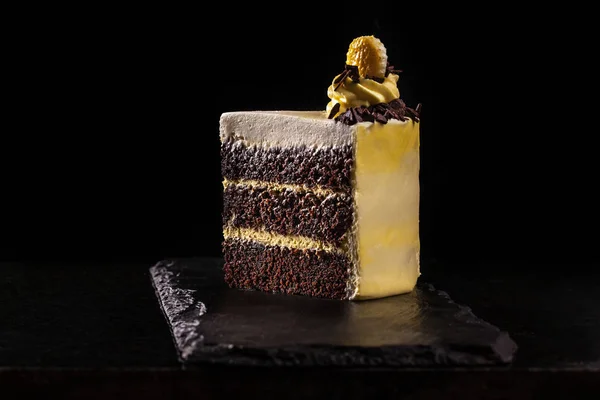 Piece of yellow birthday cake. Decorative cream decorations on the cake. Black background.