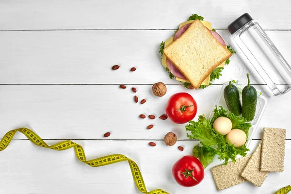 Sandviç ve taze sebze, şişe su, fındık ve yumurta beyaz ahşap zemin üzerinde öğle yemeği kutuları. Kopya alanı ile üstten görünüm