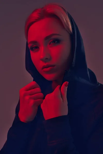 Mujer bonita joven con capucha negra y pantalones cortos sobre fondo oscuro. Retrato — Foto de Stock