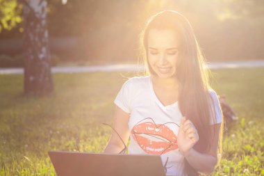 Parkta yeşil çimenler üzerinde bilgisayar kullanan genç kadın. Eğitim öğrenme ya da açık çalışma serbest ya da gevşeme kavram fikir arka plan. Güneş parlaması