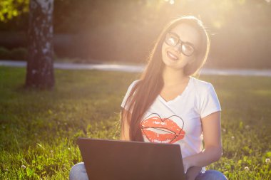 Parkta yeşil çimenler üzerinde bilgisayar kullanan genç kadın. Eğitim öğrenme ya da açık çalışma serbest ya da gevşeme kavram fikir arka plan. Güneş parlaması