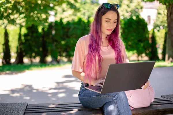 Jeune fille étudie dans le parc de printemps, assis sur le banc en bois et naviguant sur son ordinateur portable — Photo