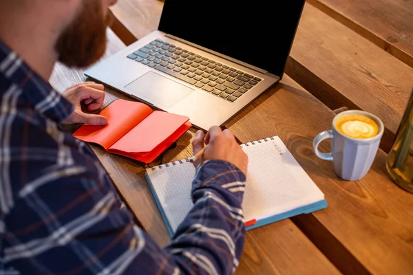 Imagem recortada de homem de negócios casual ou freelancer planejando seu trabalho no notebook, trabalhando no computador portátil com telefone inteligente, xícara de café na mesa no café ou escritório em casa . — Fotografia de Stock