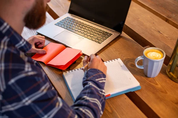 Geçici iş adamı veya serbest meslek sahibi eserleri üstünde defter, planlama ile akıllı telefon, kahve kahve dükkanı veya ev ofis, masada dizüstü bilgisayar üzerinde çalışan görüntü kırpılmış. — Stok fotoğraf