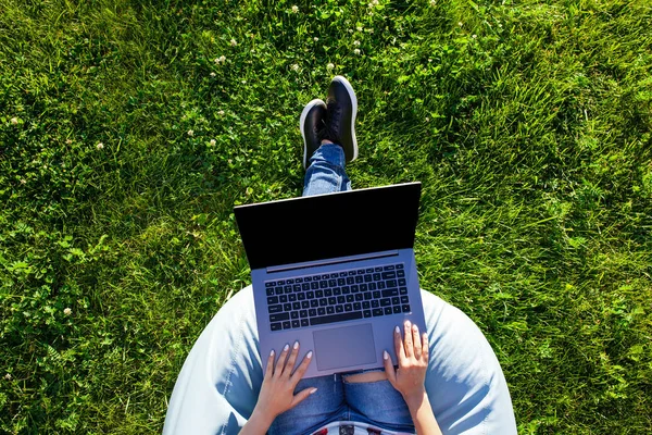 Vista dall'alto. Donna che lavora su computer portatile pc con schermo vuoto nero vuoto per copiare lo spazio nel parco su erba verde prato all'aperto . — Foto Stock