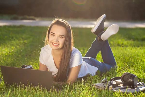 Giovane donna che utilizza il computer portatile nel parco sdraiato sull'erba verde. Tempo libero concetto di attività. — Foto Stock