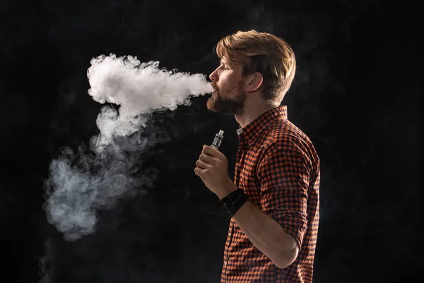 Um jovem com barba e um penteado elegante em uma camisa, fumando um cigarro, uma víbora, um quarto, um estúdio, fumaça, prazer — Fotografia de Stock