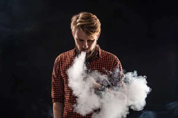 Un giovane con la barba e un'acconciatura elegante in camicia, fumando una sigaretta, una vipera, una stanza, uno studio, fumo, divertimento — Foto Stock