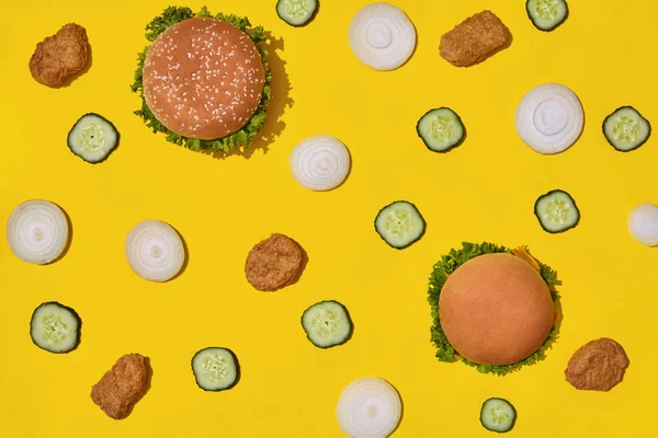 Most popular fast food meal. Chicken nuggets, burgers with fresh cucumber and onions on yellow background top view