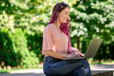 Genç kız tahta bankta oturan ve onu laptop tarama bahar Park eğitimi alıyor