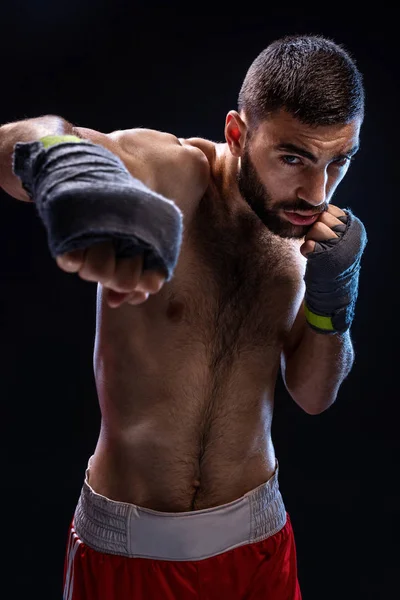 El boxeador está listo para dar un golpe poderoso. Foto de un hombre musculoso con manos fuertes y puños apretados en rayas azules sobre fondo negro . — Foto de Stock