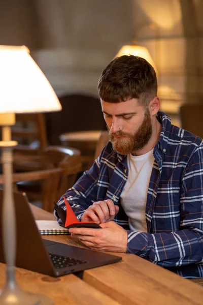 Alkalmi üzletember vagy szabadúszó tervezési munkája, notebook, laptop számítógép-val szúró telefon, csésze kávét a kávézóban, vagy otthoni irodai asztal dolgozik. — Stock Fotó