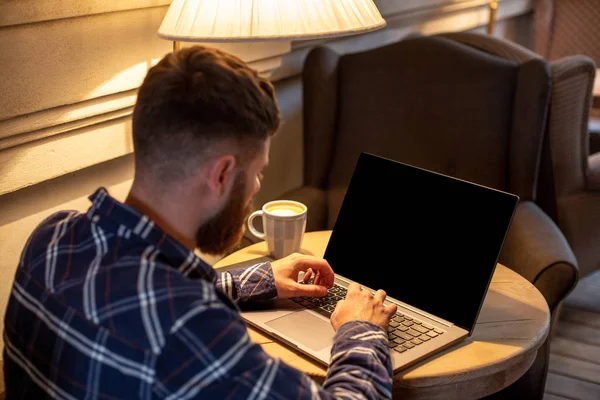 Hombre joven charlando a través de net-book durante el descanso de trabajo en la cafetería, hombre sentado en la computadora portátil abierta frontal con pantalla de espacio de copia en blanco . — Foto de Stock