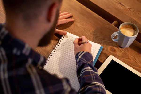 Joven hombre de negocios barbudo se sienta en la cafetería, casa en la mesa y escribe en el portátil, cerca se encuentra el ordenador tableta con pantalla negra. El hombre está trabajando, estudiando . — Foto de Stock