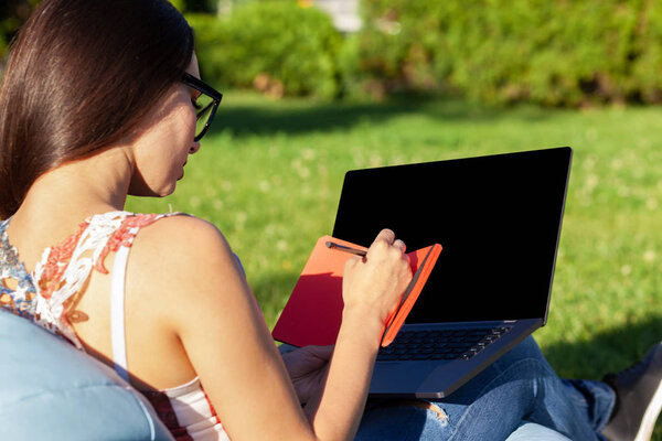 Close up hands on keyboard. Woman working on laptop pc computer with blank black empty screen to copy space in park on green grass sunshine lawn outdoors.