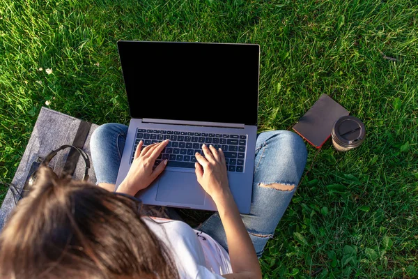 Vista dall'alto. Donna che lavora su computer portatile pc con schermo vuoto nero vuoto per copiare lo spazio nel parco su erba verde prato all'aperto . — Foto Stock