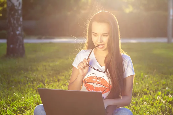 Jeune femme utilisant un ordinateur sur les herbes vertes dans le parc. Éducation apprentissage ou freelance travailler en plein air ou de détente concept idée arrière-plan. Éclair de soleil — Photo