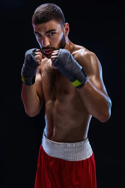 Boxing man ready to fight. Boxer with strong hands and clenched fists in blue straps against a black background