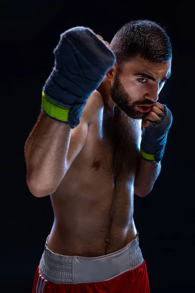 Boxing man ready to fight. Boxer with strong hands and clenched fists in blue straps against a black background