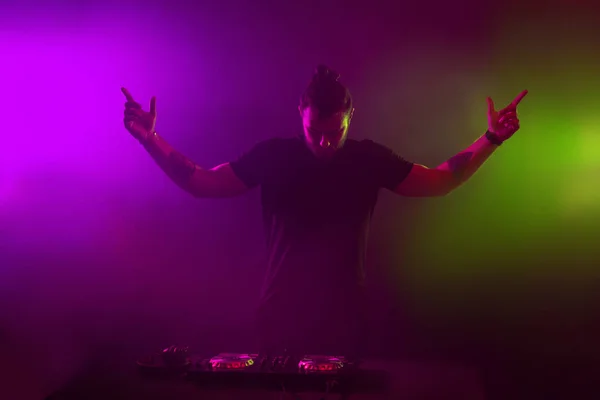 DJ at work mixing sound on her decks at a party or night club with colourful smoke light background — Stock Photo, Image