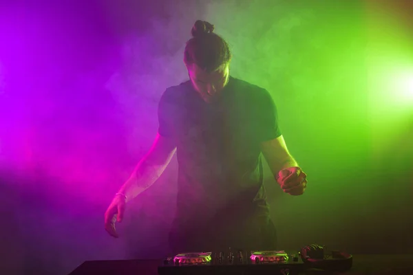 DJ на роботі змішуючи звук на палубах у вечірньому або нічному клубі з барвистим фоном диму — стокове фото