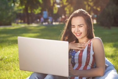 Fasulye çanta kullanmak laptop güneş Park'ta çimenlerin üzerinde dinlenme süre oturan genç ve güzel kadın