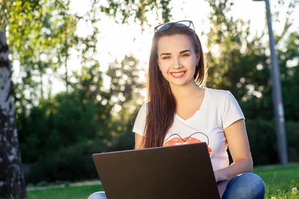 Молодая женщина использует компьютер на зеленых травах в парке. Обучение или внештатная работа под открытым небом или идея релаксации . — стоковое фото