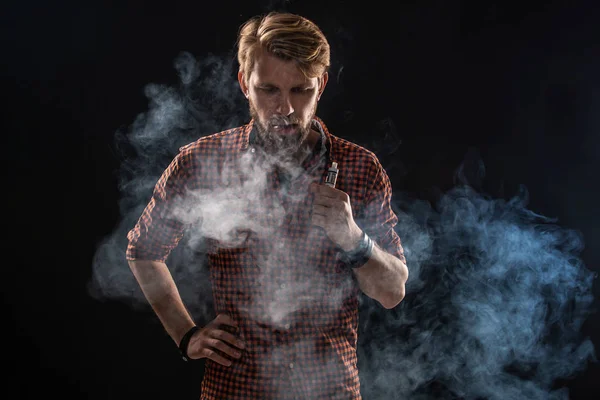 Un joven con barba y un peinado elegante con camisa, fumando un cigarrillo, una víbora, una habitación, un estudio, humo, disfrute — Foto de Stock