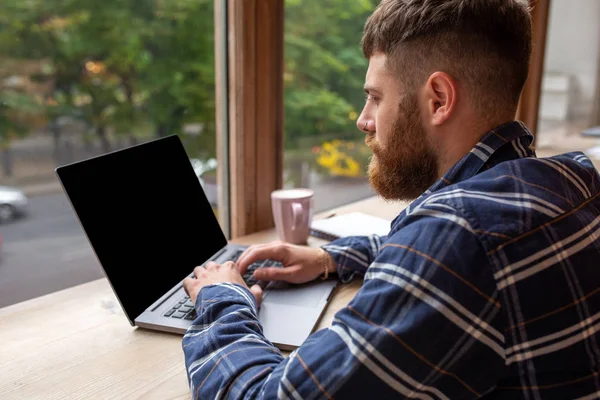 Hombre joven charlando a través de net-book durante el descanso de trabajo en la cafetería, hombre sentado en la computadora portátil abierta frontal con pantalla de espacio de copia en blanco . — Foto de Stock