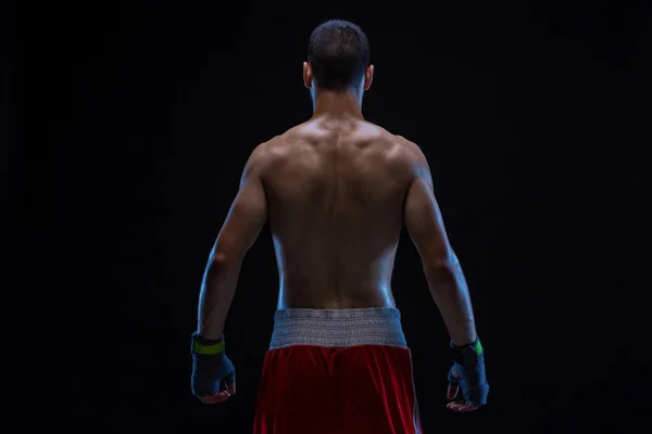 Rear view of strong young male boxer. Fitness male model wearing boxing gloves standing on black background.