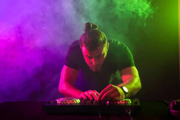 Atractiv tânăr DJ joc pe mese turnante cu efecte de lumină de culoare — Fotografie, imagine de stoc