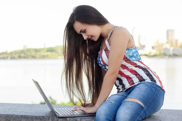 Красивая молодая женщина сидит в парке возле реки с ноутбуком . — стоковое фото