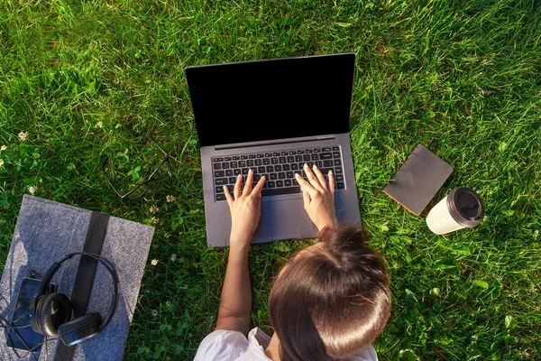 Vista dall'alto. Donna che lavora su computer portatile pc con schermo vuoto nero vuoto per copiare lo spazio nel parco su erba verde prato all'aperto . — Foto Stock