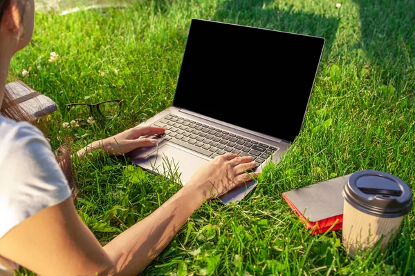 Chiudi le mani sulla tastiera. Donna che lavora su computer portatile pc con schermo vuoto nero vuoto per copiare lo spazio nel parco su erba verde prato all'aperto . — Foto Stock