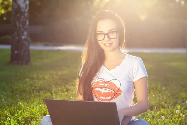 Jeune femme utilisant un ordinateur sur les herbes vertes dans le parc. Éducation apprentissage ou freelance travailler en plein air ou de détente concept idée arrière-plan. Éclair de soleil — Photo