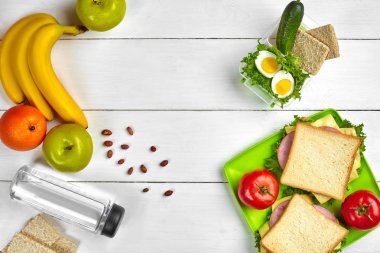 Öğle Yemeği. Sandviç ve taze sebze, şişe su, fındık ve meyve Beyaz ahşap zemin üzerinde. Sağlıklı beslenme kavramı. Kopya alanı ile üstten görünüm