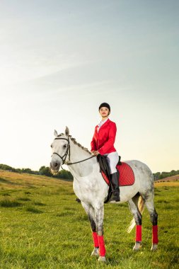 Kırmızı redingote ve gün batımı ışık akşam içinde onun atı ile beyaz pantolon giyen genç kadın binici.