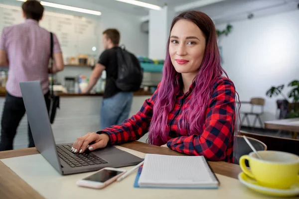 Jeune femme aux cheveux roses avec ordinateur portable assis dans un café, étudiante intelligente travaillant sur le net-book . — Photo