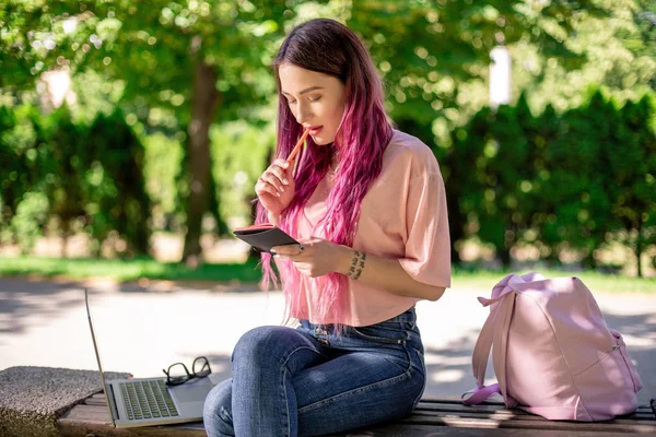 Frau, die in einem Notizbuch auf einer Holzbank im Park sitzt. Mädchen arbeitet im Freien auf tragbarem Computer, Kopierraum. — Stockfoto
