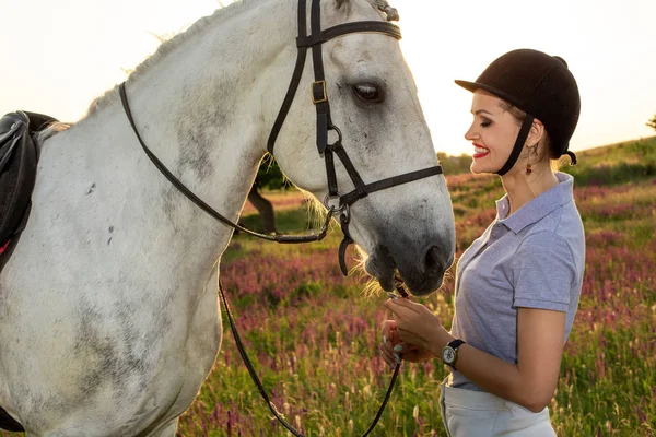 Jockey young girl petting and hugging white horse in evening sunset — Stock Photo, Image