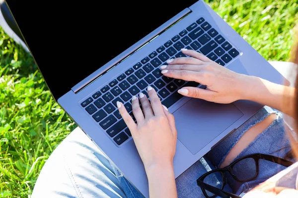 Close up hands on keyboard. Woman working on laptop pc computer with blank black empty screen to copy space in park on green grass sunshine lawn outdoors.