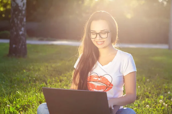 Молода жінка використовує комп'ютер на зелених травах в парку. Освіта навчання або позаштатна робота на відкритому повітрі або концепція релаксації фону. Сонячне полум'я — стокове фото