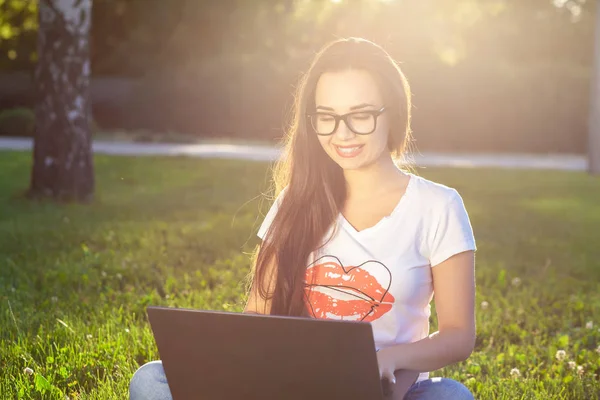 Jeune femme utilisant un ordinateur sur les herbes vertes dans le parc. Éducation apprentissage ou freelance travailler en plein air ou de détente concept idée arrière-plan. Éclair de soleil — Photo