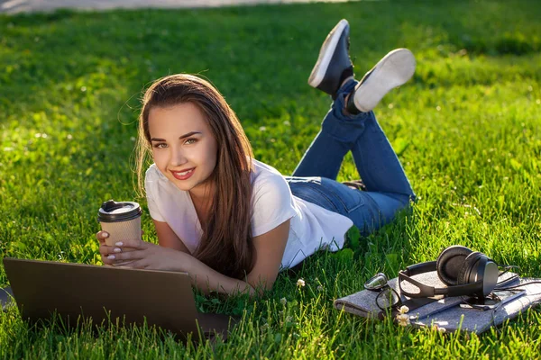 Mladá žena používající notebook v parku ležící na zelené trávě. Koncept volnočasové aktivity. — Stock fotografie