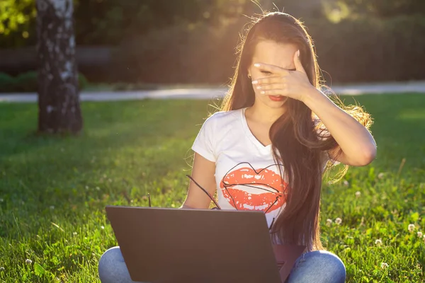 Молодая женщина использует компьютер на зеленых травах в парке. Обучение или внештатная работа на открытом воздухе или концепция релаксации фон. Солнечная вспышка — стоковое фото