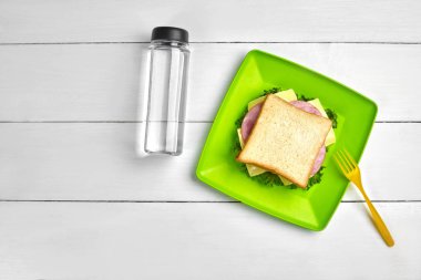 Peynir ve jambonlu sandviç, şişe su beyaz ahşap masa üzerinde. Sağlıklı öğle yemeği fikir kavramı