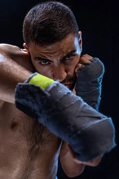 El boxeador está listo para dar un golpe poderoso. Foto de un hombre musculoso con manos fuertes y puños apretados en rayas azules sobre fondo negro . —  Fotos de Stock